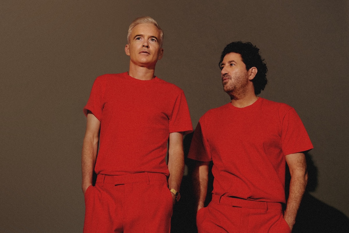 Australian electronic music duo The Avalanches posing together wearing matching bright red outfits against a dark backdrop.